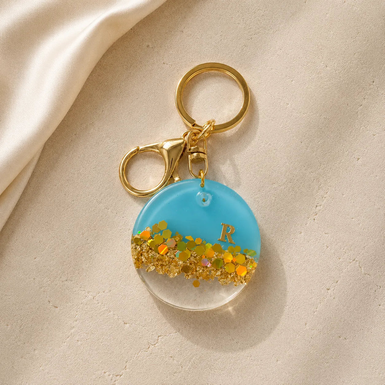 Keychain with blue round charm featuring gold glitter and letter 'R' on a beige background