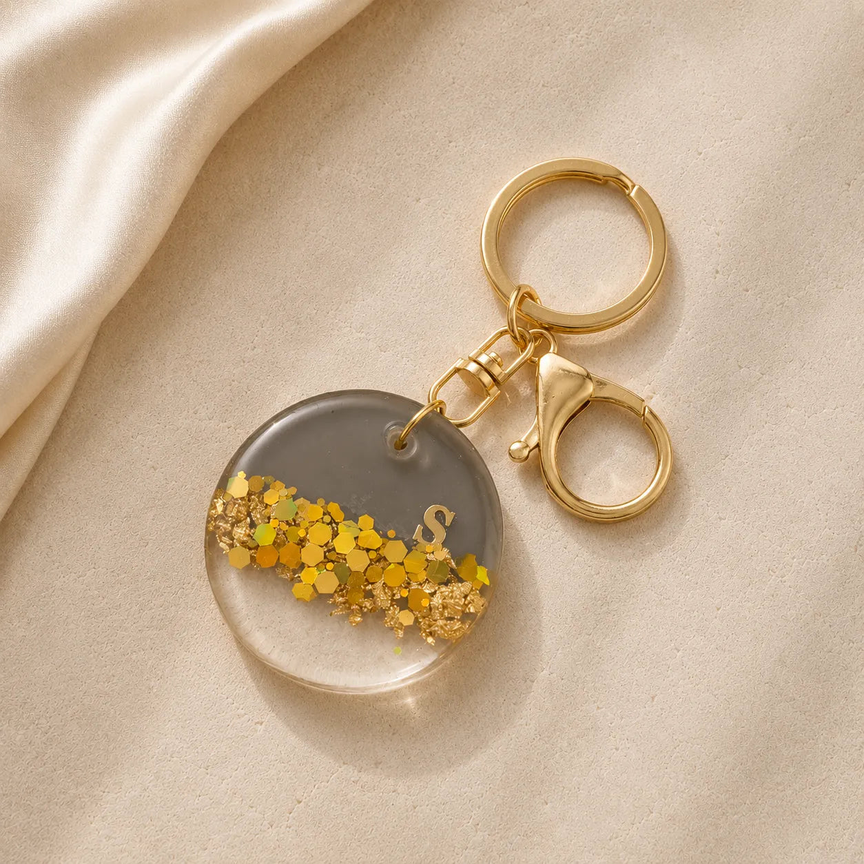 Keychain with gold glitter and letter 'S' on a beige fabric background