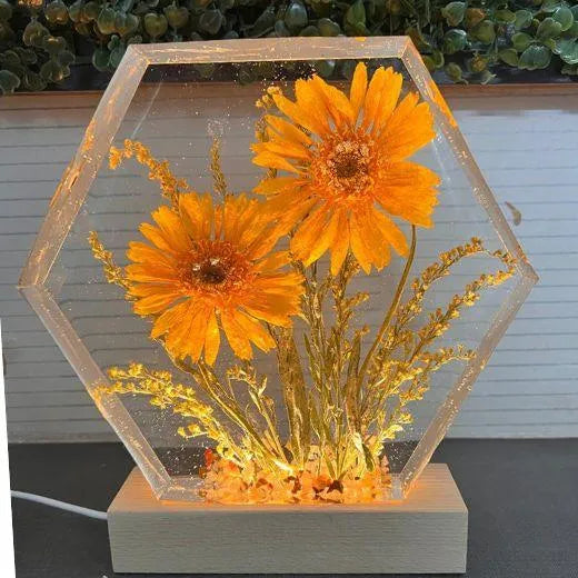 Hexagonal glass container with glowing yellow flowers on a wooden base.