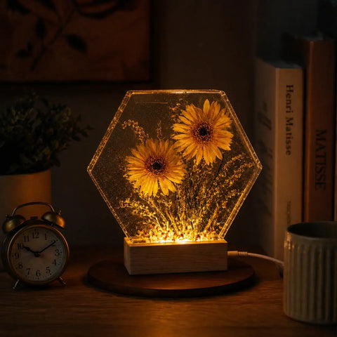Hexagonal LED night light with sunflowers on a wooden base in a dimly lit room.