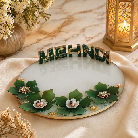 Decorative plate with 'MEHNDI' letters on a marble surface with flowers and a lantern.