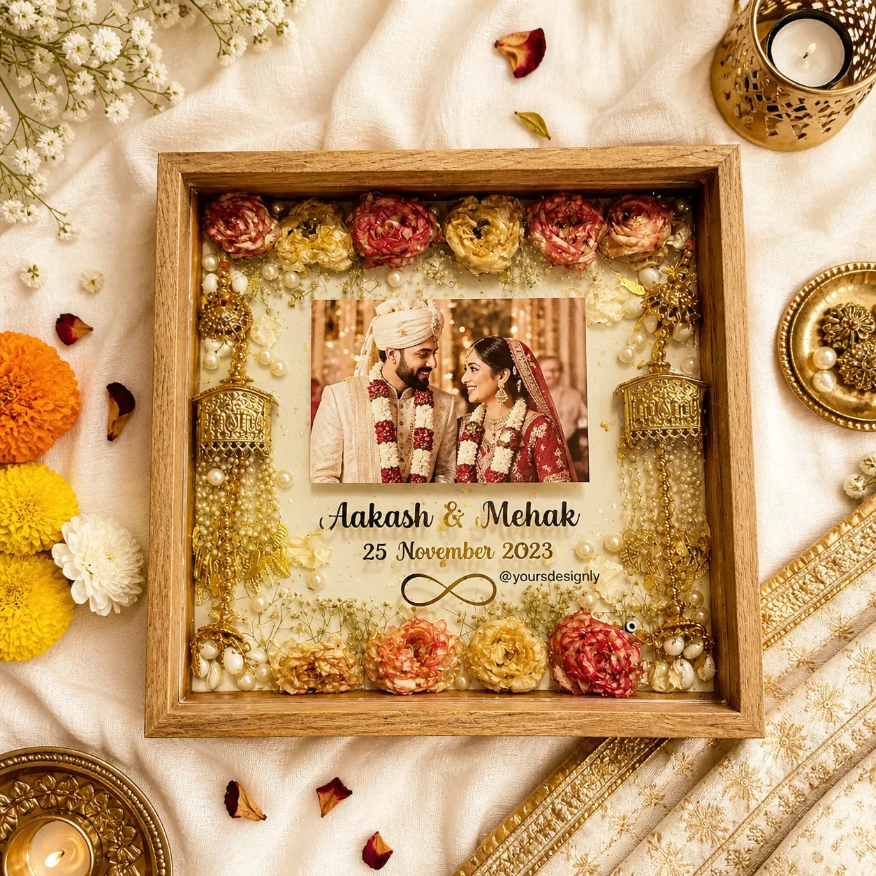 Decorative frame with flowers and jewelry, featuring a photo of a couple on a white fabric background.
