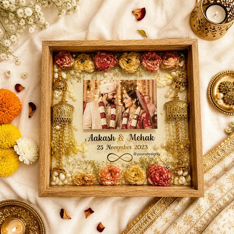 Decorative frame with flowers and jewelry, featuring a photo of a couple on a white fabric background.