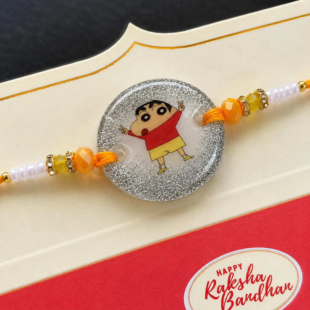 Decorative rakhi with cartoon character on a card with 'Happy Raksha Bandhan' text.