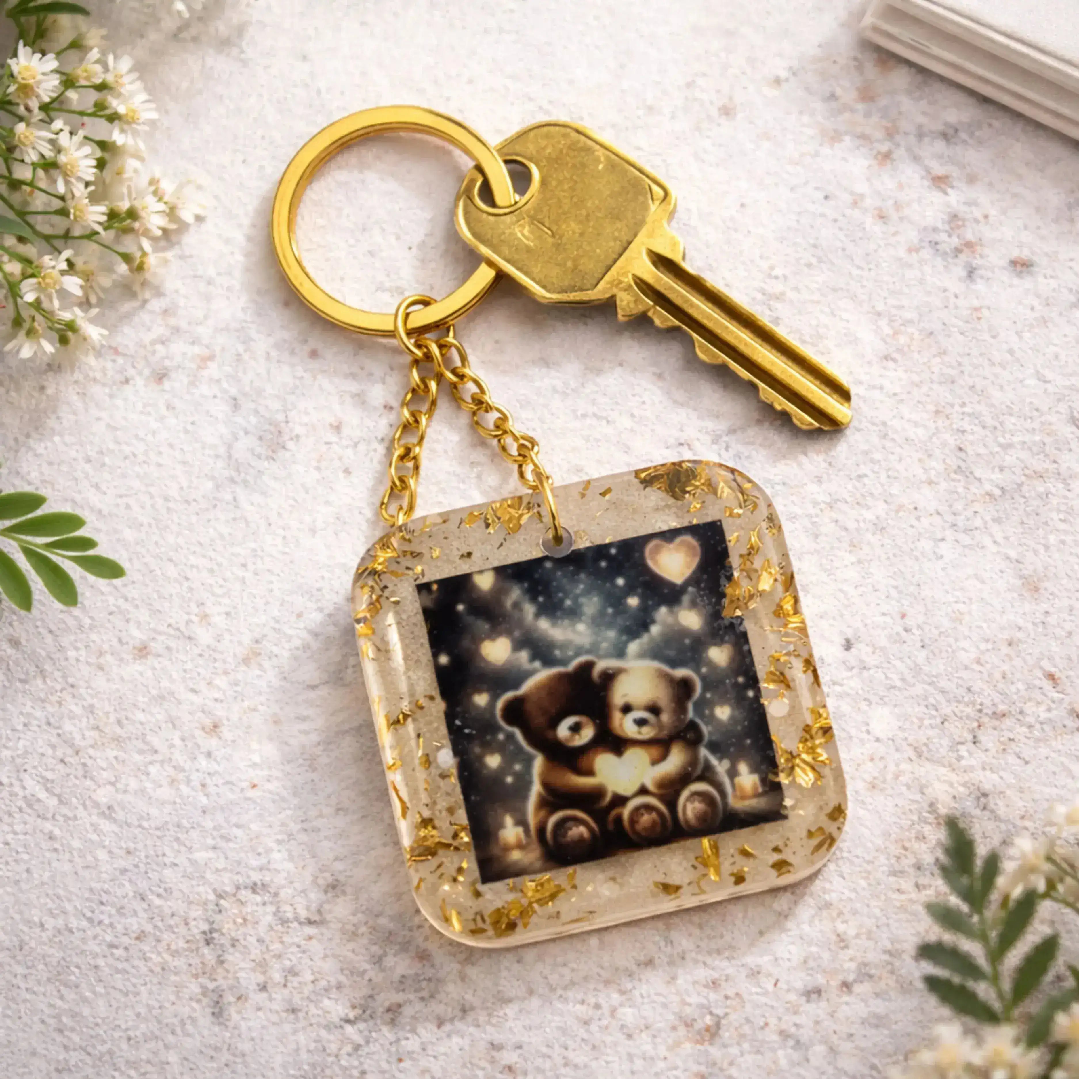 Keychain with a teddy bear design on a light surface with flowers and leaves.