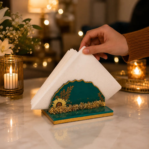 Decorative paper towel holder with a hand pulling out a towel, set against a warm, blurred background with candles and flowers.