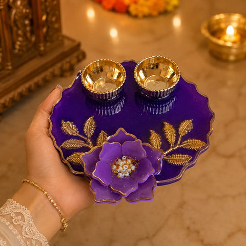 Decorative purple plate with gold floral design held by a hand, with a blurred background of lights and objects.