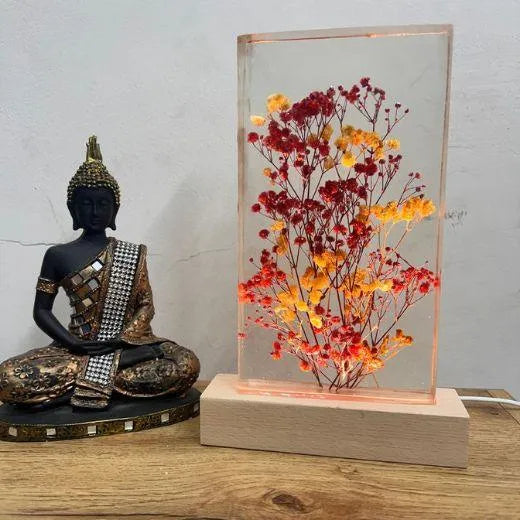 Decorative lamp with flowers and a Buddha statue on a wooden surface.