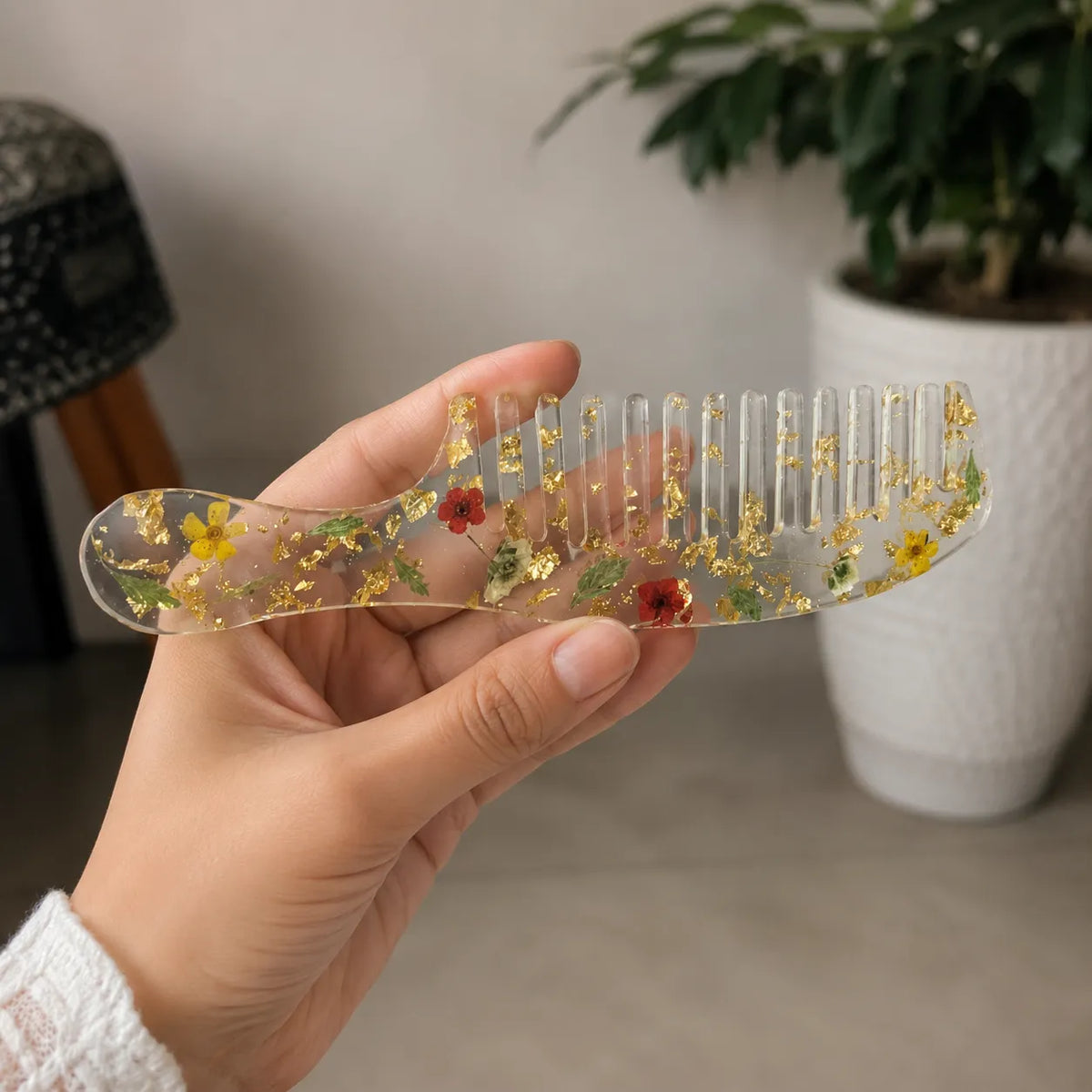 Hand holding elegant floral resin hair comb with real dried flowers, gold foil detailing, and crystal-clear glossy finish.