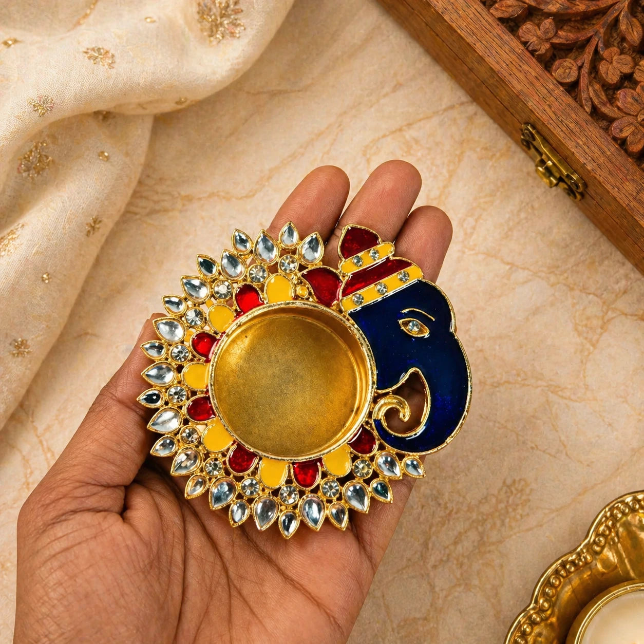 Decorative diya with colorful design held by a hand on a textured fabric background