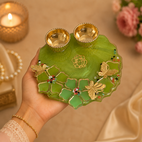 Hand holding a green decorative plate with gold accents and two small bowls, against a warm-toned background.