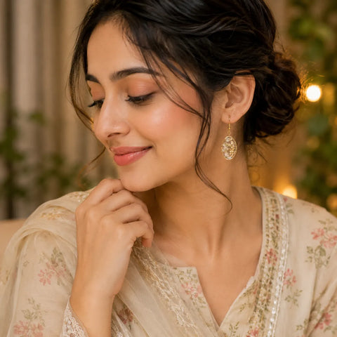 Indian woman wearing floral resin oval drop earrings with white dried flowers, gold flakes, and elegant gold border design