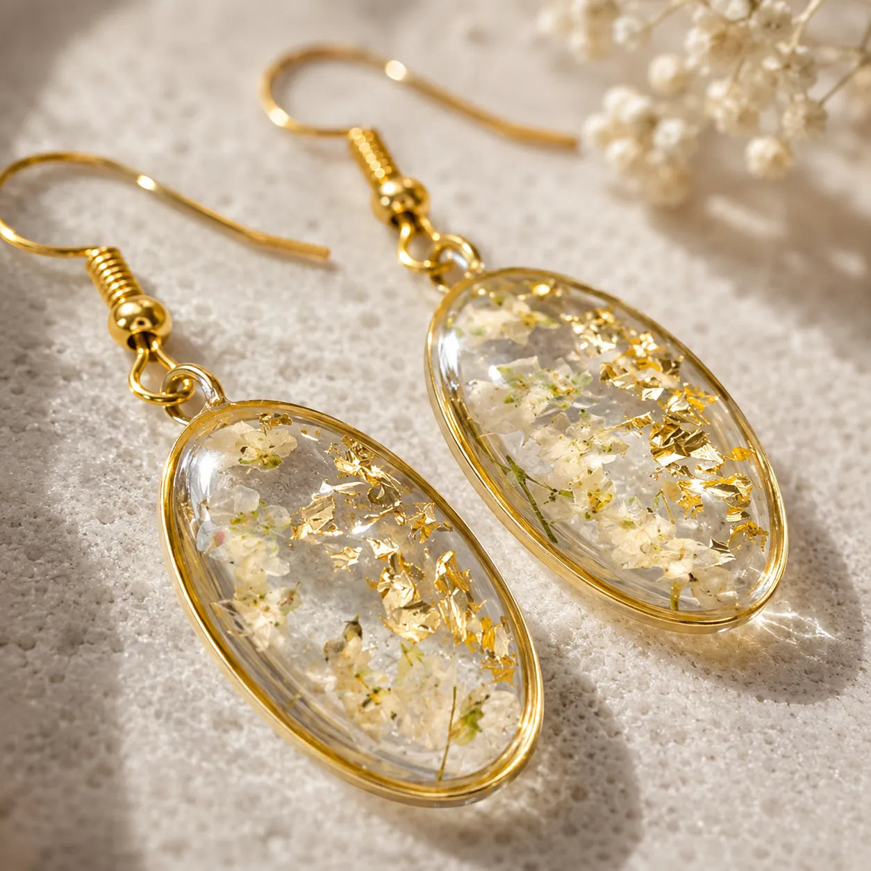 Gold-framed earrings with clear resin and gold leaf on a textured surface