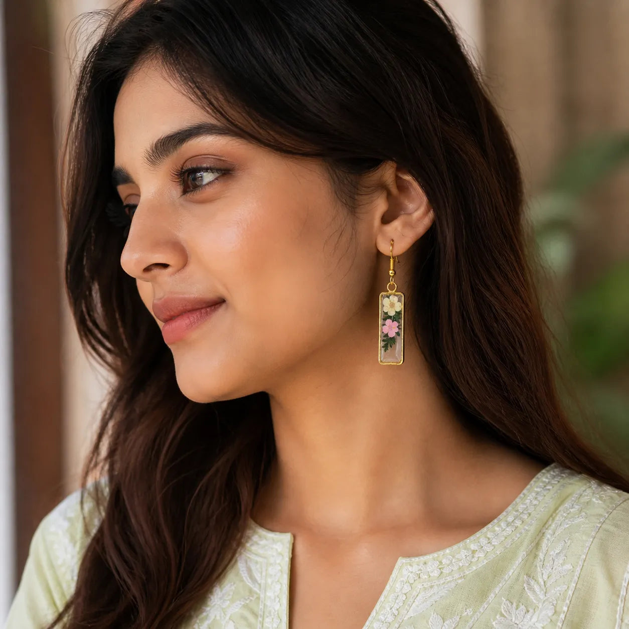 Indian woman wearing floral resin rectangle drop earrings with white and pink dried flowers in an elegant handmade botanical jewellery style