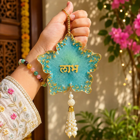 Decorative star-shaped ornament with 'Laxmi' text held by a hand wearing a bracelet, with a floral background.