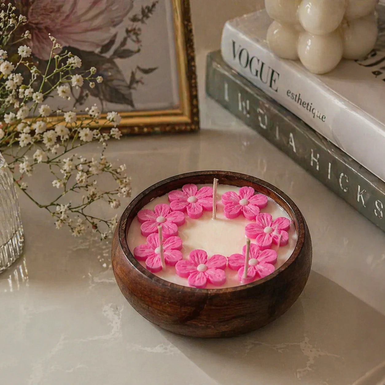Candle with pink floral designs in a wooden bowl on a marble surface.
