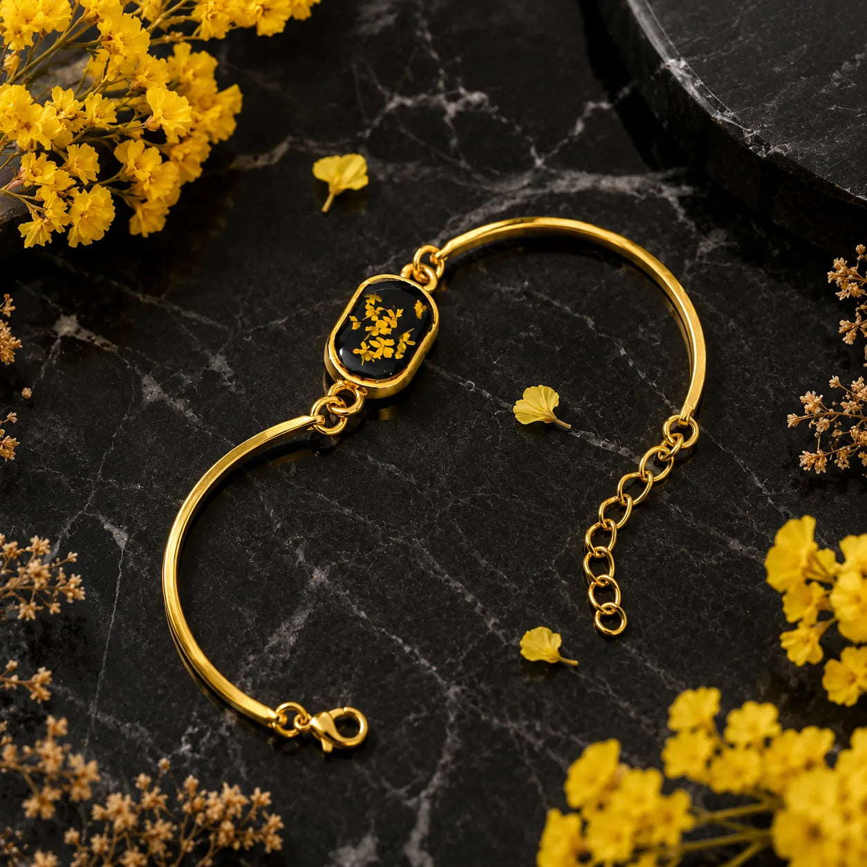 Gold bracelet with a clasp on a black marble surface with yellow flowers.