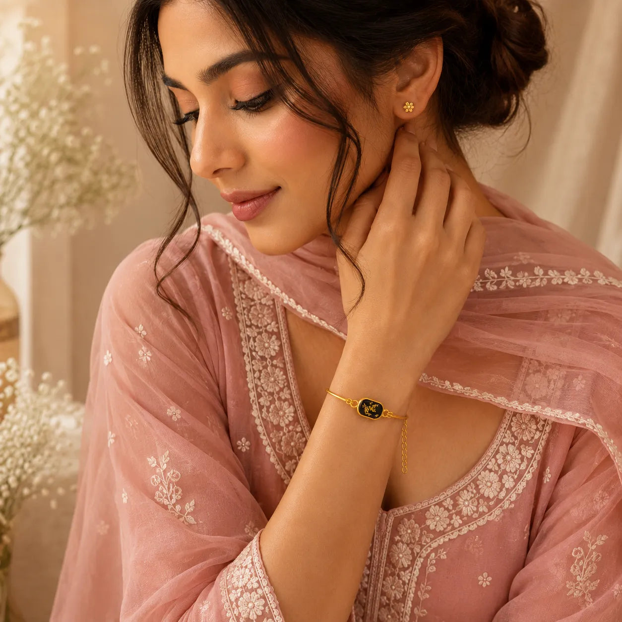 Woman wearing a pink embroidered saree with jewelry, sitting indoors.