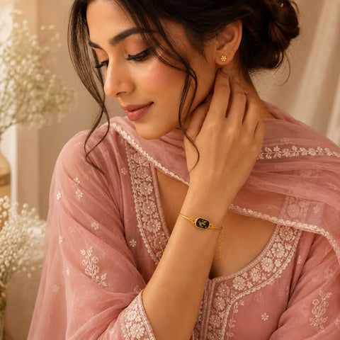 Woman wearing a pink embroidered saree with jewelry, sitting indoors.