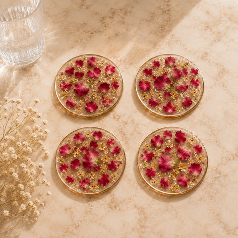 Four round floral coasters with red flowers and gold accents on a beige marble surface.