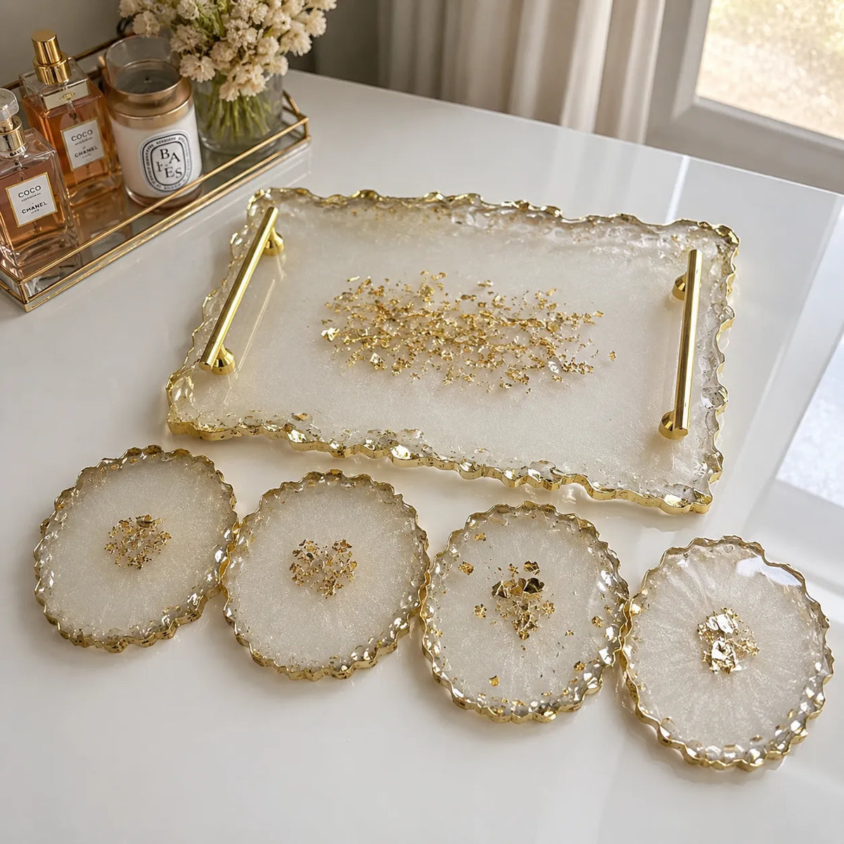 Cream white resin serving tray set with four matching coasters, featuring gold textured edges, gold handles, and elegant gold foil detailing on a glossy marble-style tabletop background.