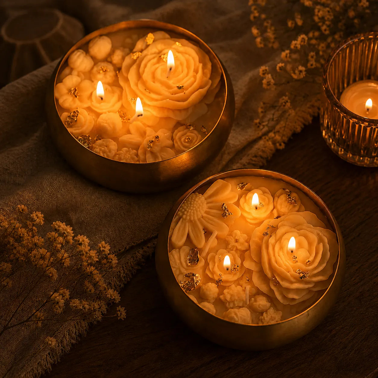 Decorative candles with floral designs in metallic holders on a textured surface.