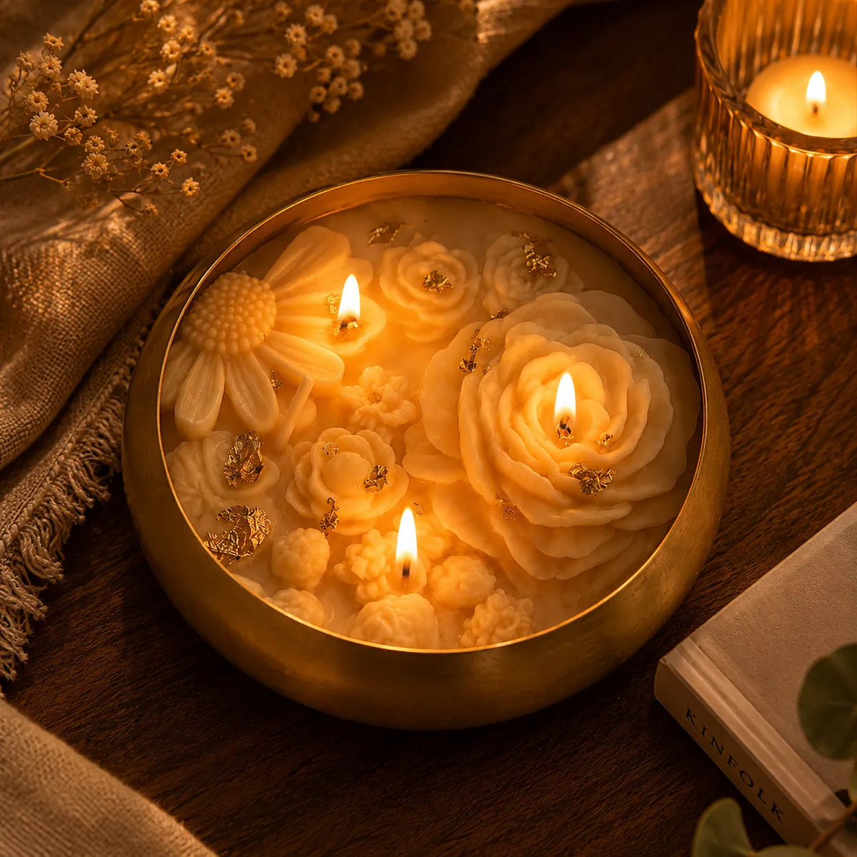 Decorative candle with floral designs in a gold holder on a wooden surface.