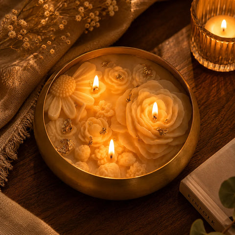 Decorative candle with floral designs in a gold holder on a wooden surface.