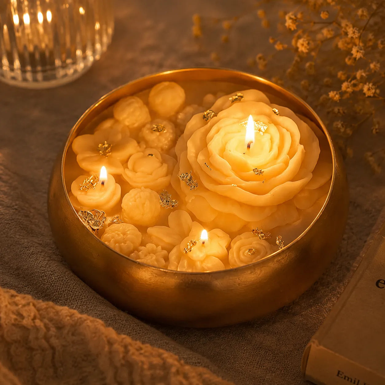 Decorative candle with rose-shaped wax pieces floating in a gold container on a textured surface.
