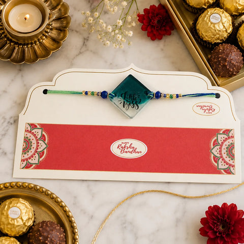 Rakhi with a card on a marble surface with chocolates and flowers.