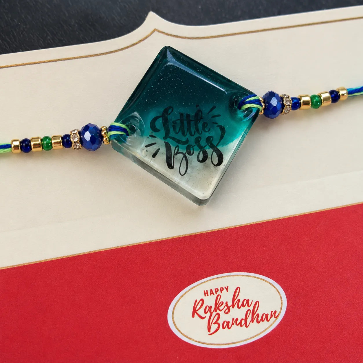 Decorative bracelet with 'Little Boss' on a red card with 'Happy Raksha Bandhan' text.