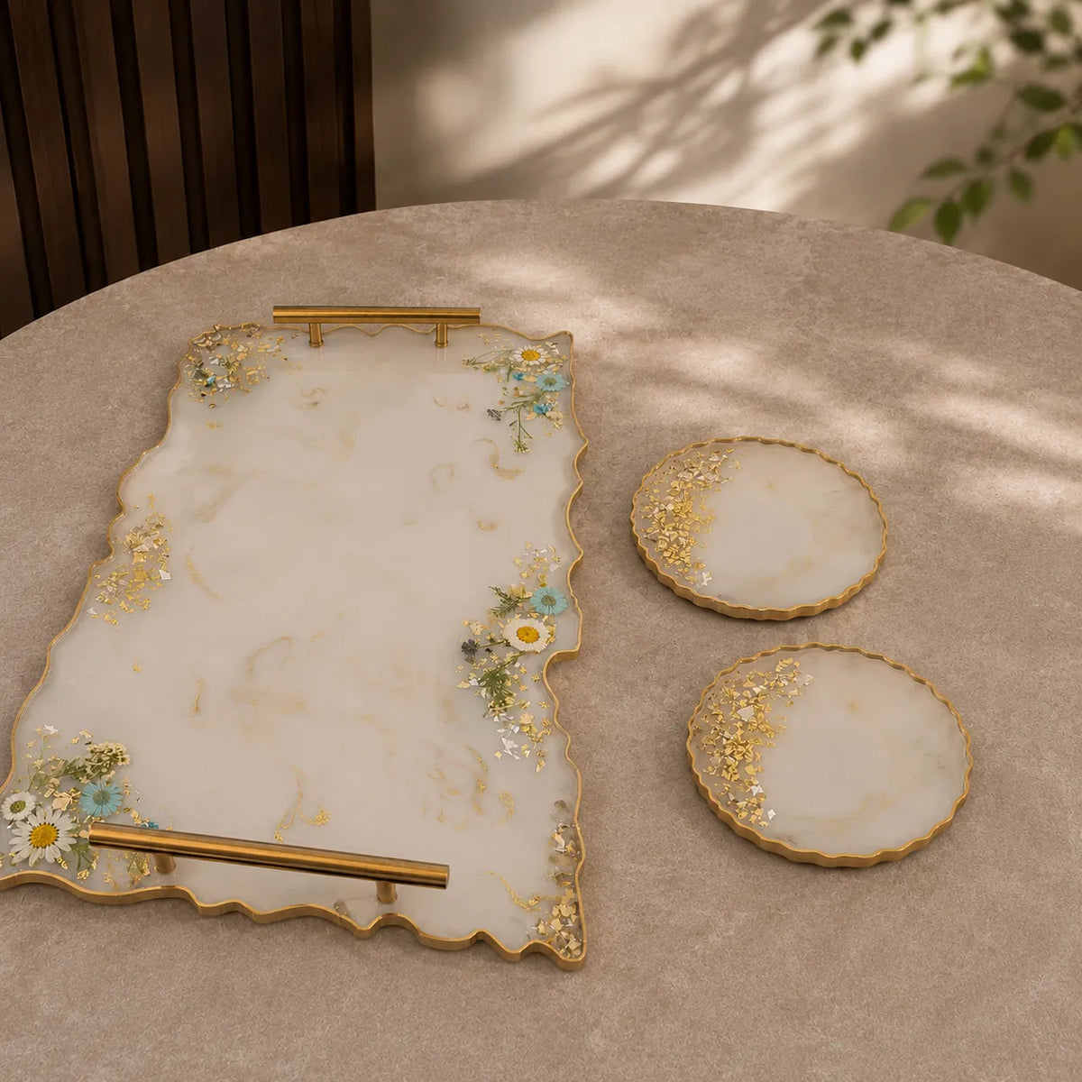 Cream marble resin serving tray with gold handles and matching round coasters featuring gold flakes, white daisy floral detailing, and luxury handmade glossy finish on a premium beige table setup.