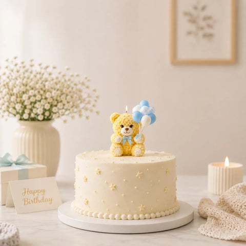 White birthday cake with a teddy bear topper on a table with decorative elements.
