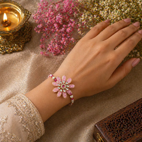 Hand wearing a pink floral bracelet on a decorative surface with flowers and a lit candle.