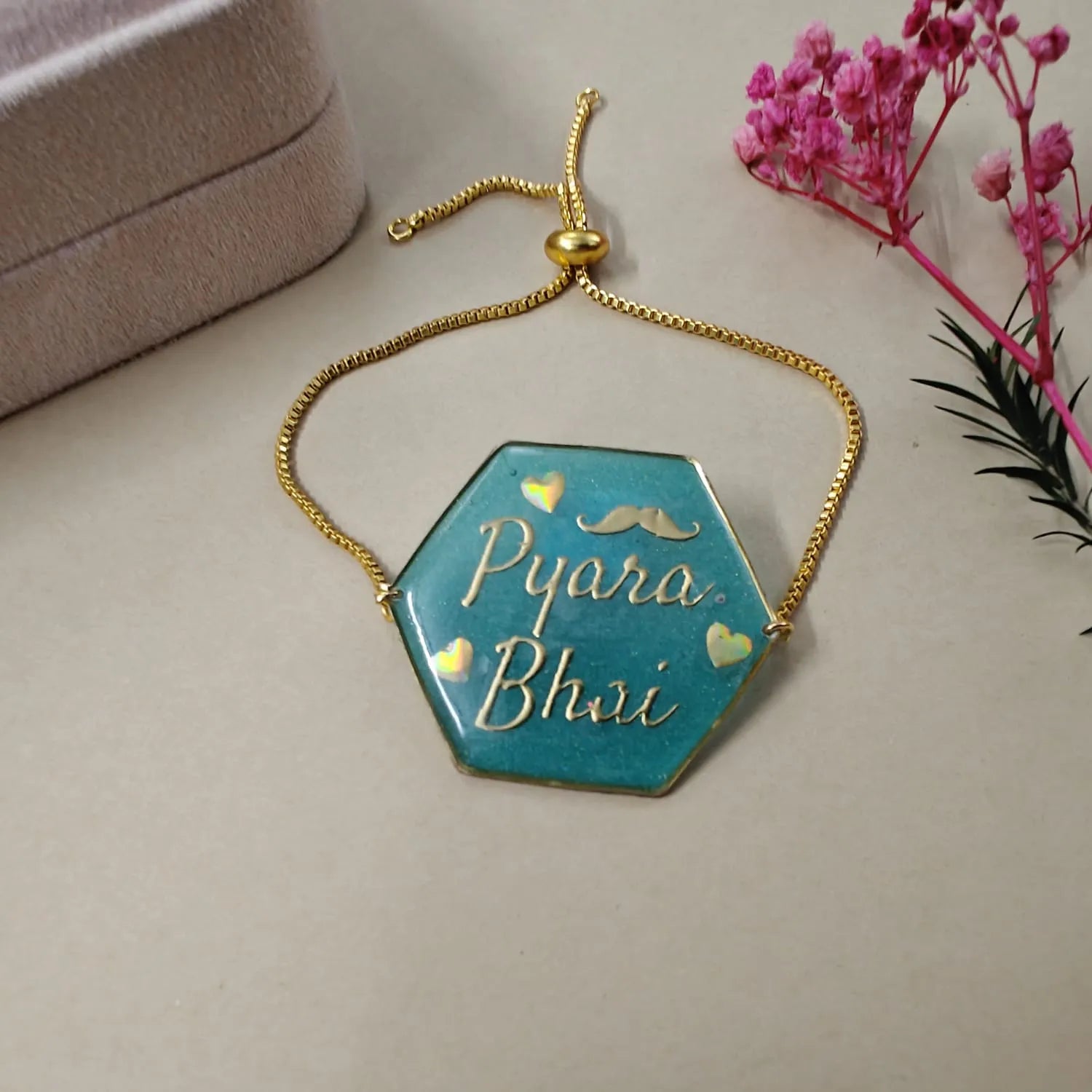 Hexagonal blue pendant with gold chain on a light surface with pink flowers in the background