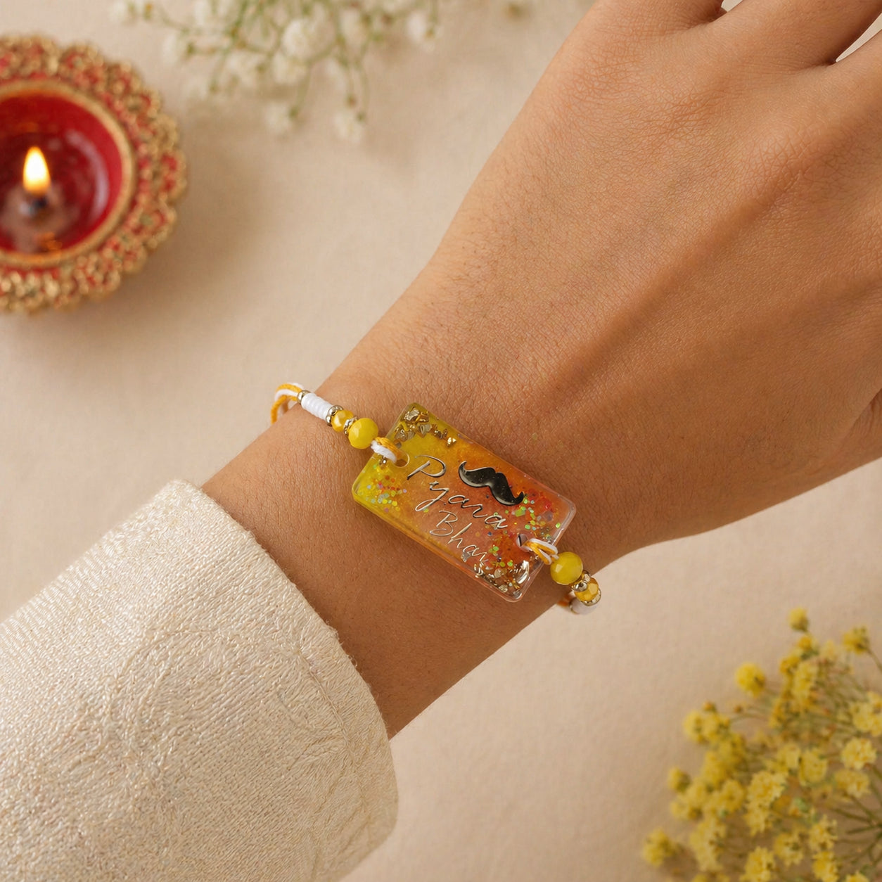 Bracelet with decorative elements on a wrist, with a blurred background of flowers and a candle.
