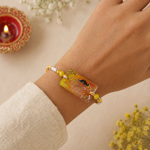 Bracelet with decorative elements on a wrist, with a blurred background of flowers and a candle.