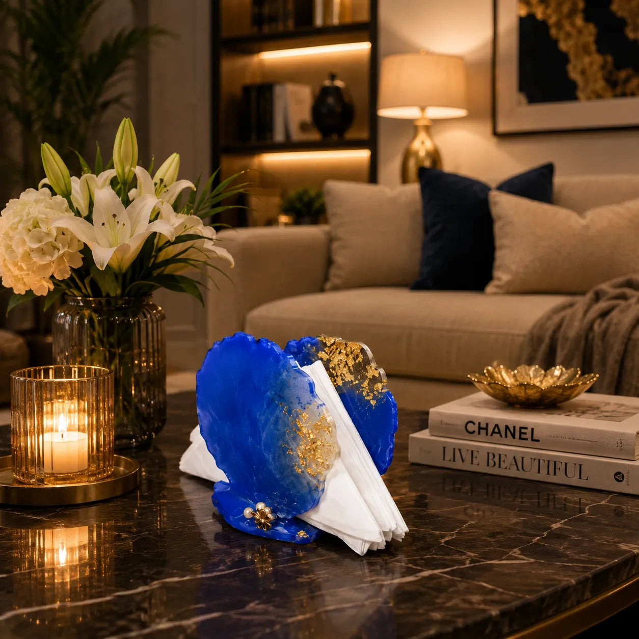 Decorative blue and gold object on a coffee table with candles, flowers, and books in a living room setting.