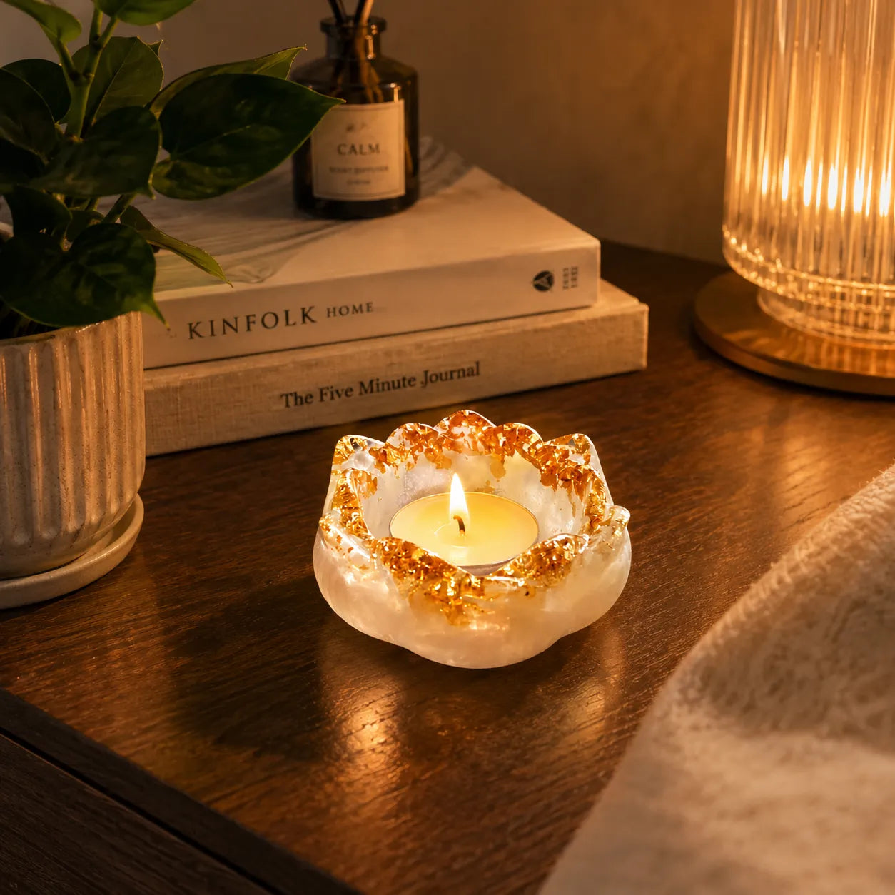 Candle in a decorative holder on a wooden surface with books and a plant in the background