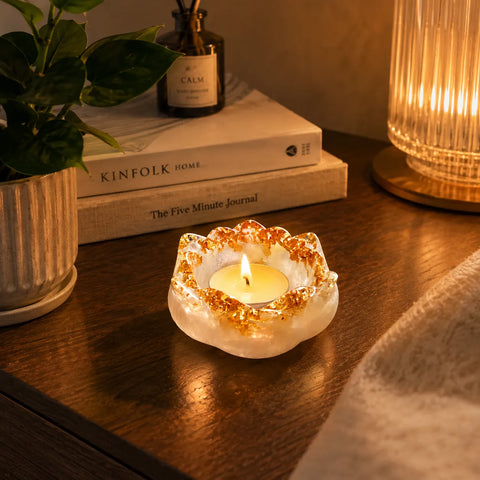 Candle in a decorative holder on a wooden surface with books and a plant in the background