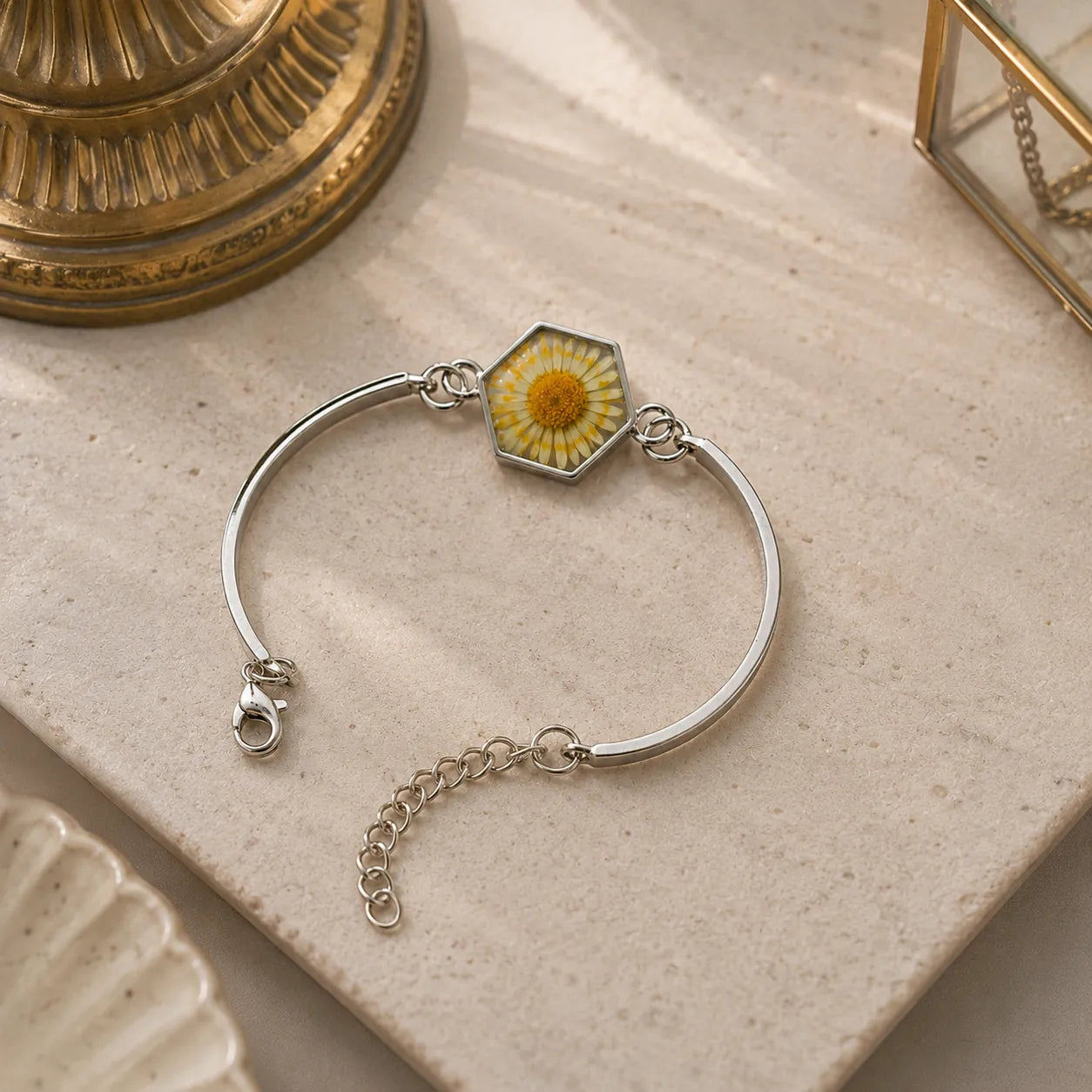 Silver bracelet with a hexagonal charm featuring a yellow flower on a textured surface.