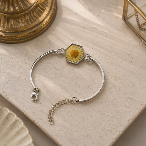 Silver bracelet with a hexagonal charm featuring a yellow flower on a textured surface.
