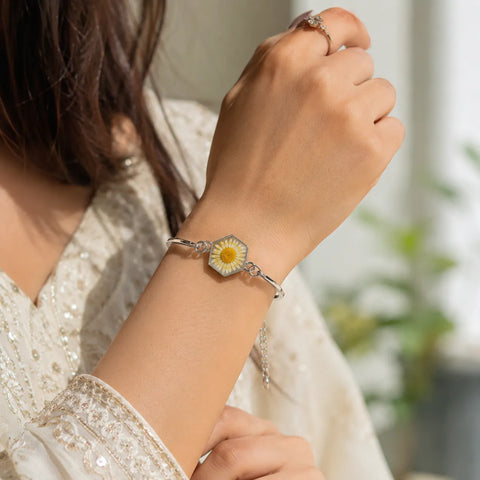 Person wearing a silver bracelet with a floral charm, blurred background