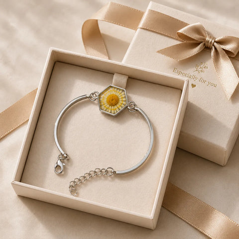 Silver bracelet with a floral charm in an open box, next to a gift box with a bow.