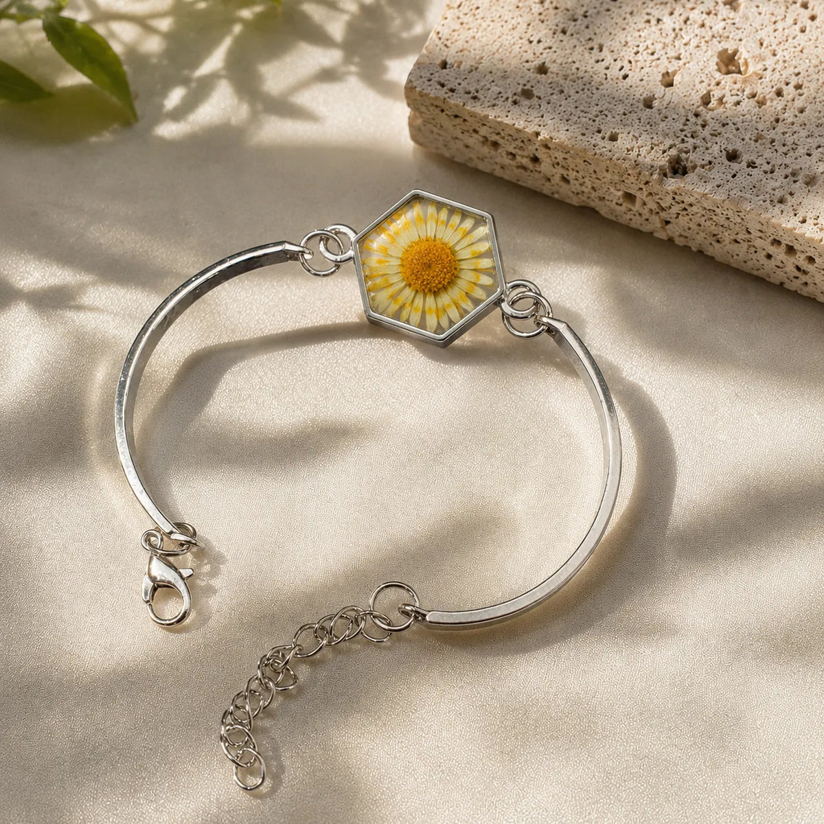 Silver bracelet with a hexagonal charm featuring a yellow flower on a beige surface.