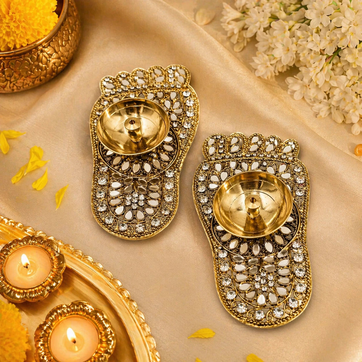 Decorative gold diya holders with candles on a beige fabric background.