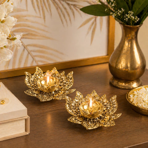 Decorative gold candle holders on a wooden surface with a vase and framed artwork in the background.