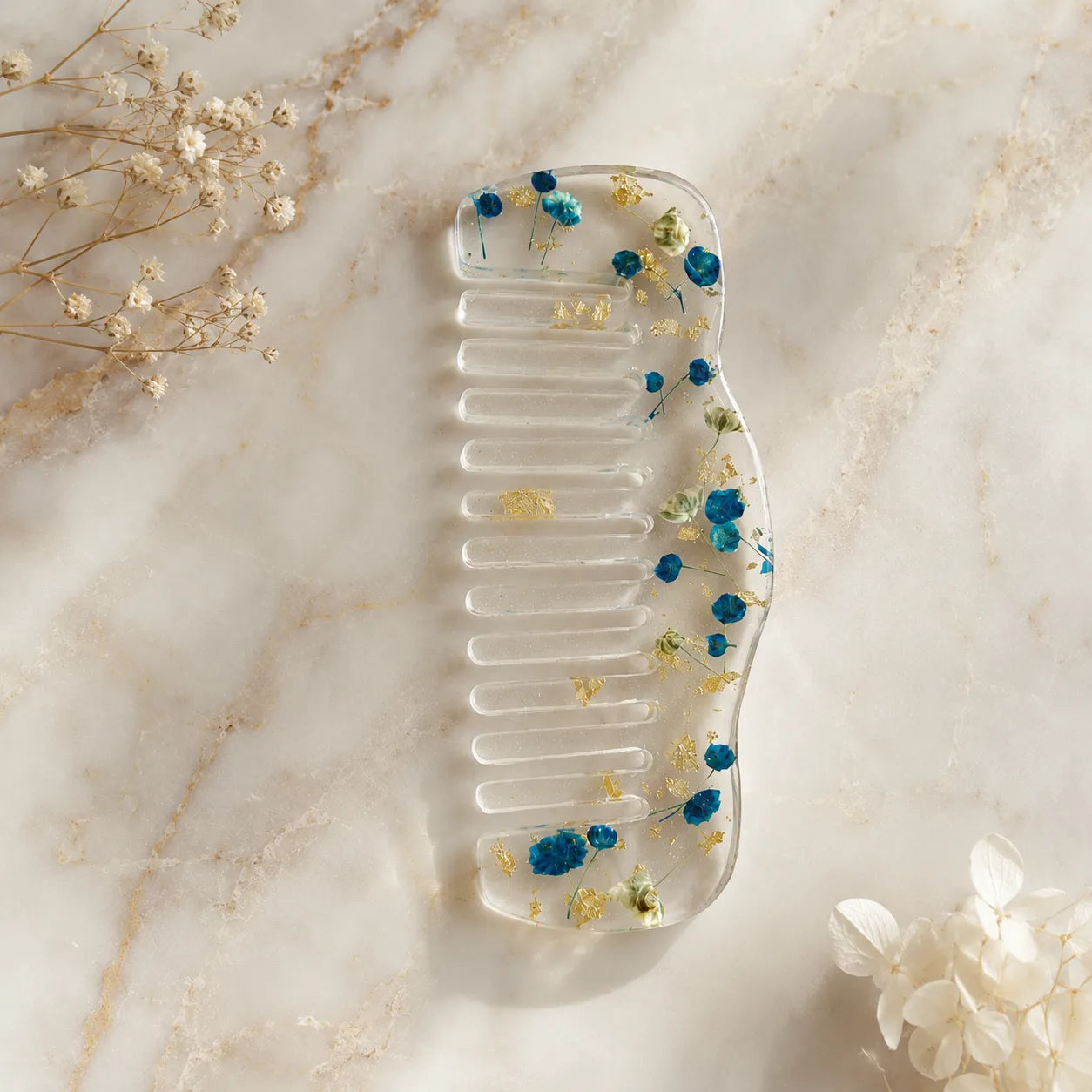 Clear comb with dried flowers on a marble surface