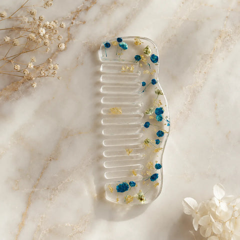 Clear comb with dried flowers on a marble surface