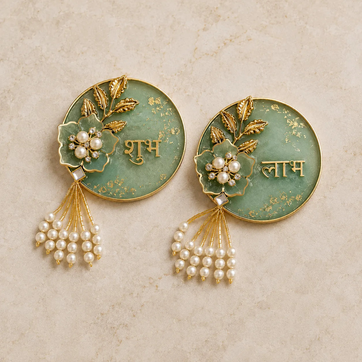 Pair of decorative earrings with green circular design, gold accents, and pearl elements on a beige background.